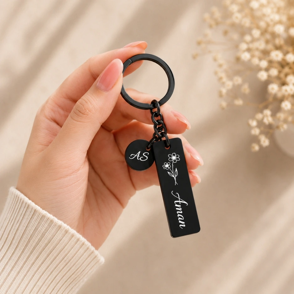 Customized black metal name keychain with engraved floral design and initials held in hand