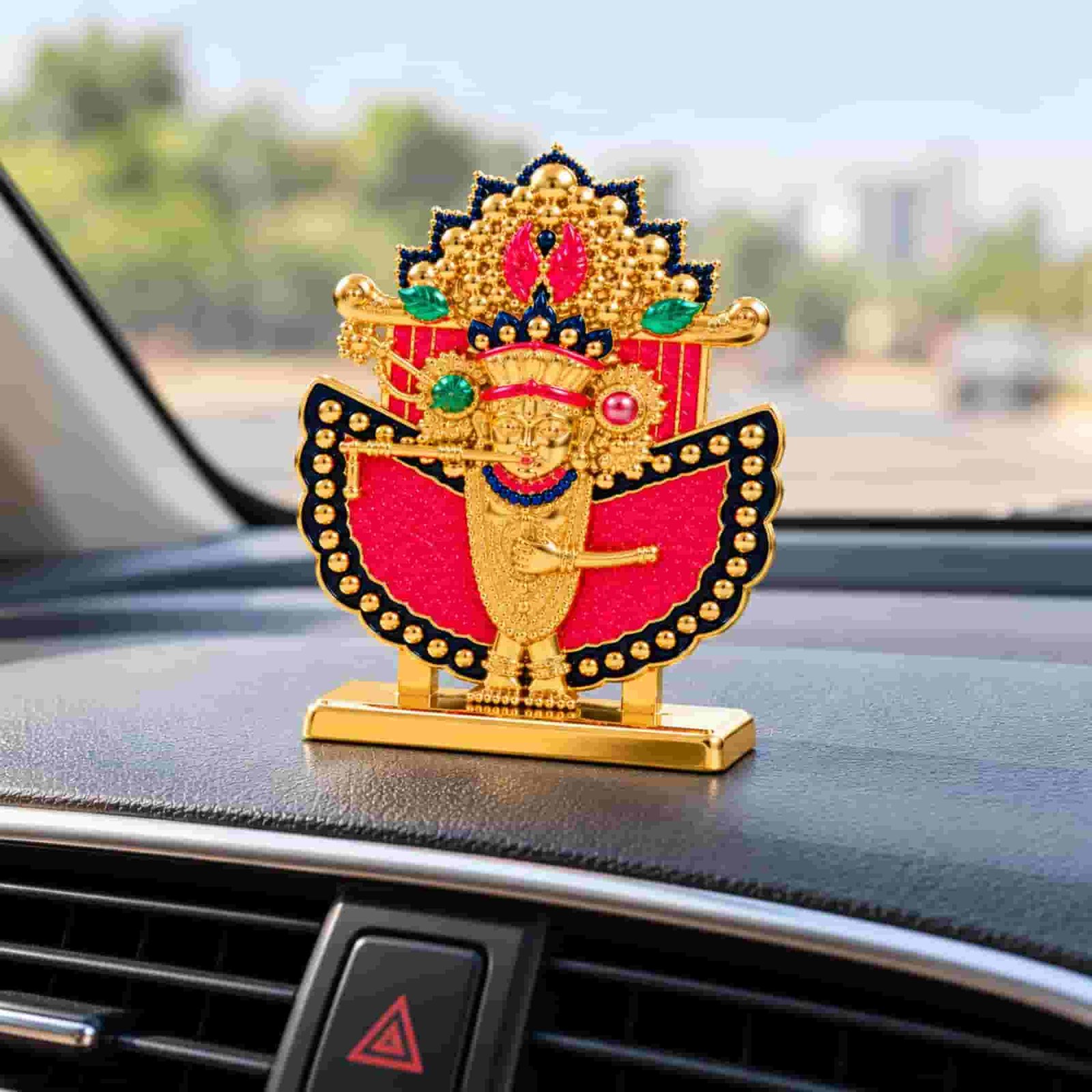 Shri Sanwaliya Seth idol with golden finish, red decorative backing, ornate crown, and rectangular base displayed on a car dashboard.