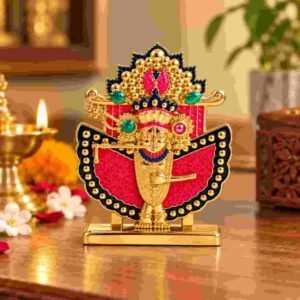 Shri Sanwaliya Seth idol with golden finish and red decorative backdrop displayed beside a lit diya in a festive pooja setting.