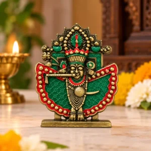 Shri Sanwaliya Seth idol in antique brass finish with green and red detailing displayed on a wooden table beside a lit diya and flowers