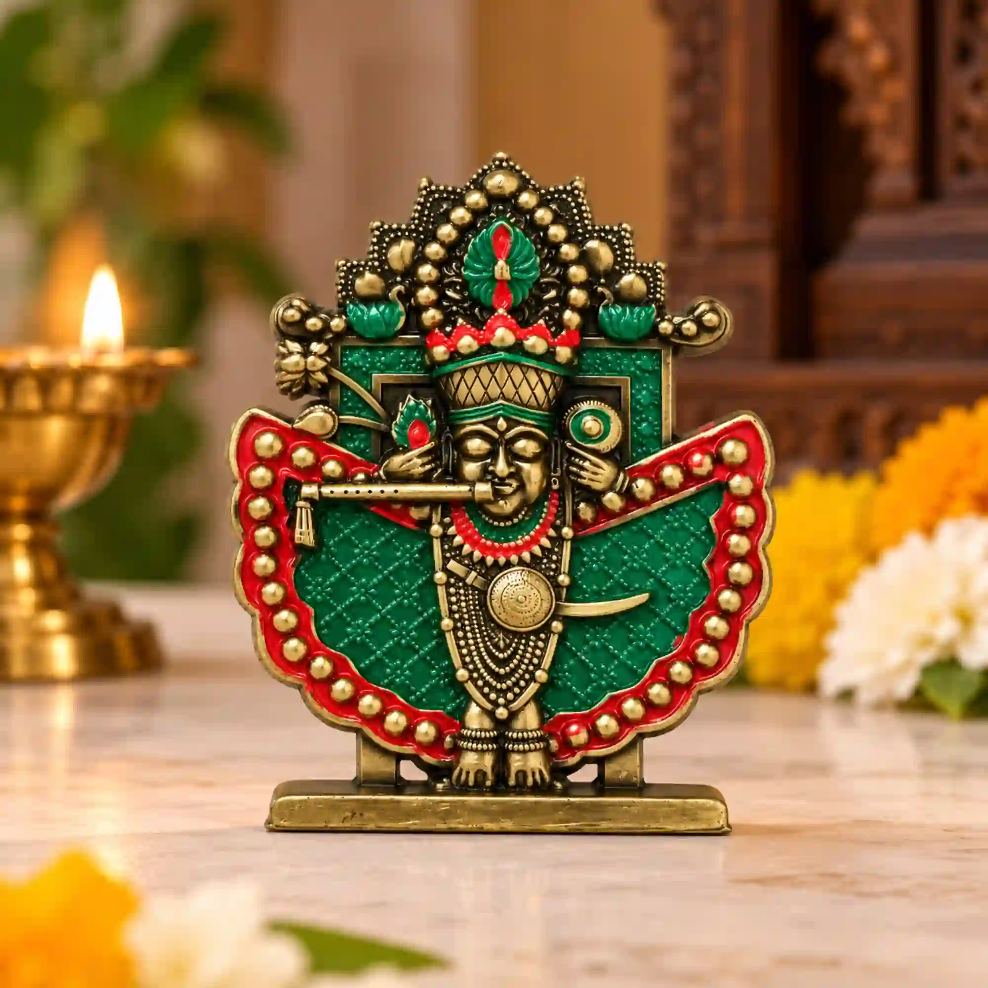 Shri Sanwaliya Seth idol in antique brass finish with green and red detailing displayed on a wooden table beside a lit diya and flowers